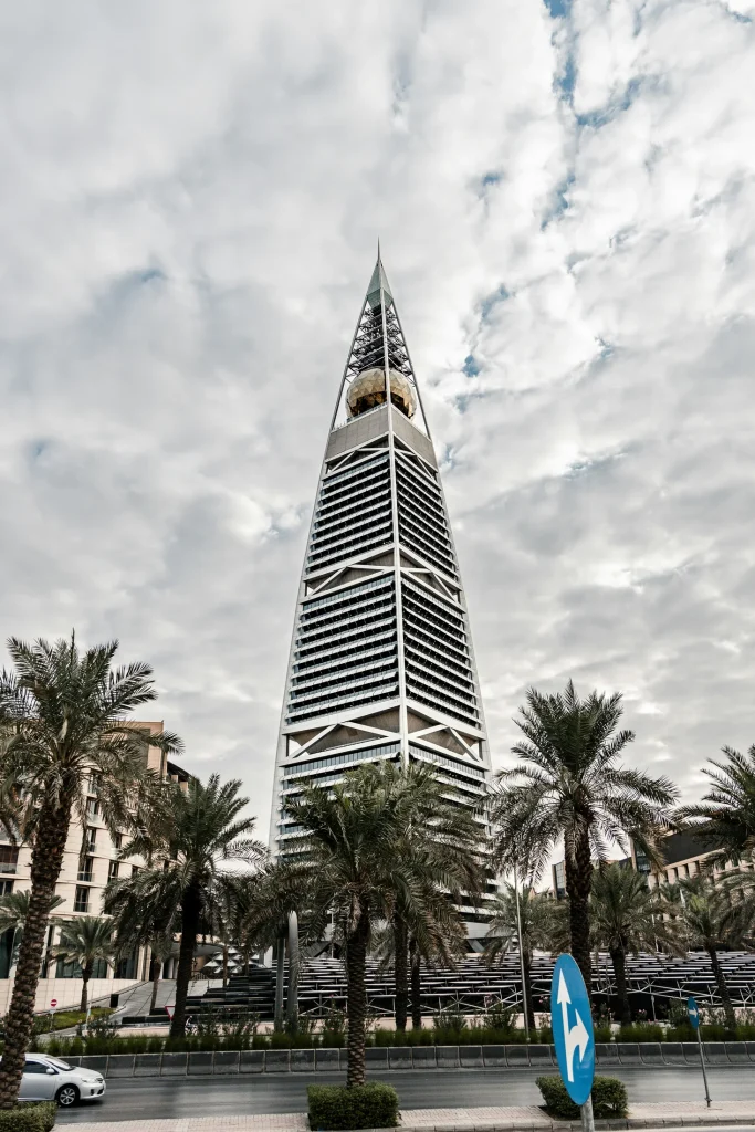 Al Faisaliah Tower framed by palm trees beneath a cloudy sky