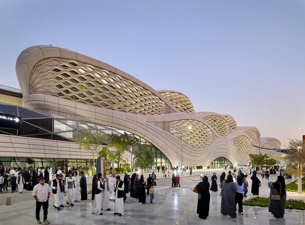 Visitors outside KAFD Metro Station beneath its flowing lattice façade at dusk