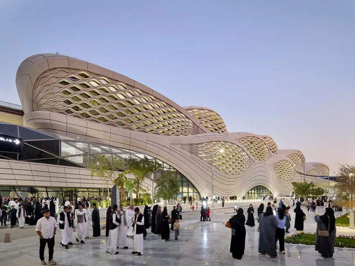 Visitors outside KAFD Metro Station beneath its flowing lattice façade at dusk