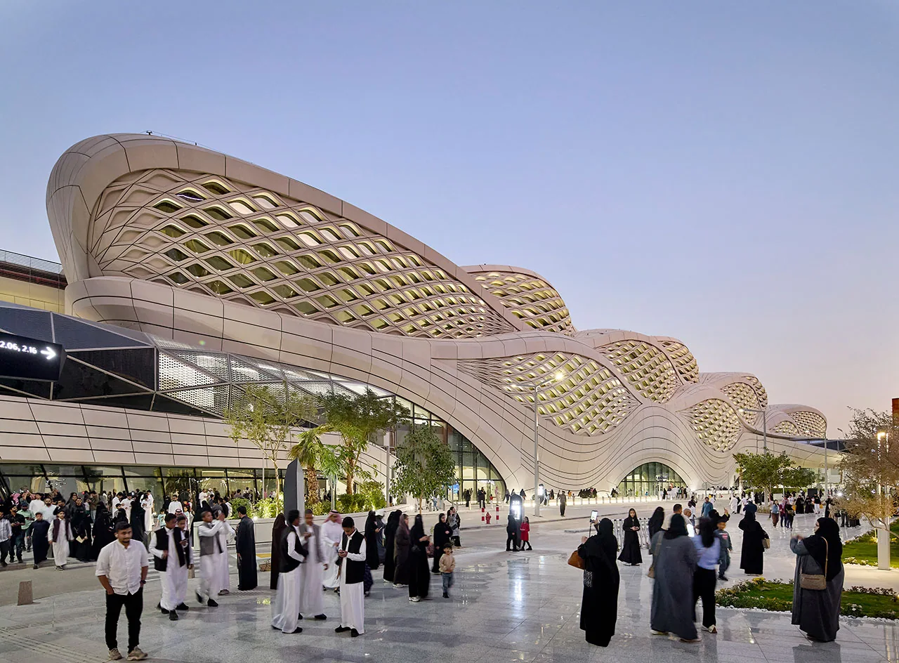 Visitors outside KAFD Metro Station beneath its flowing lattice façade at dusk