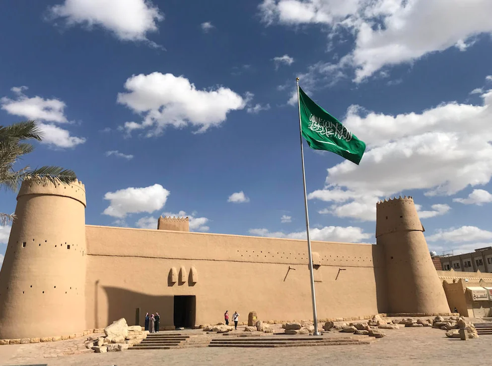 Al Masmak’s earthen walls and round towers beneath a Saudi flag and a blue sky