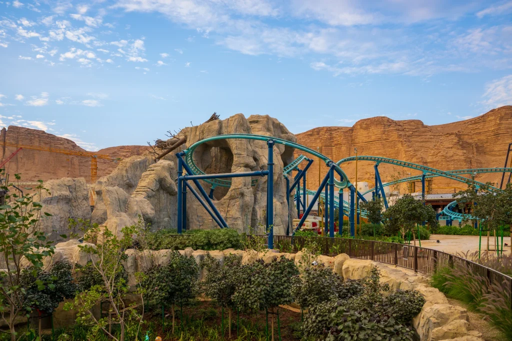 A roller coaster and landscaping beneath the Qiddiya cliffs
