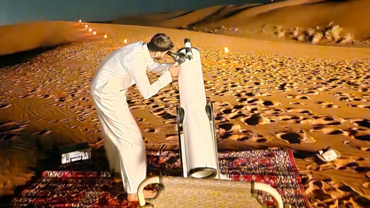 A visitor looking through a telescope on sand dunes at night.